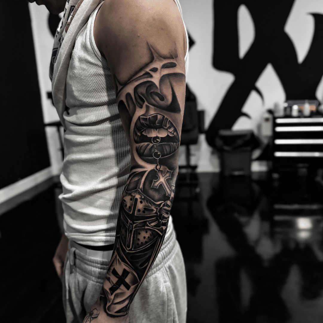 Black and grey full arm sleeve with lips, a cross pendant and a crusader helmet, Tagz Tattoo in Mesa, AZ