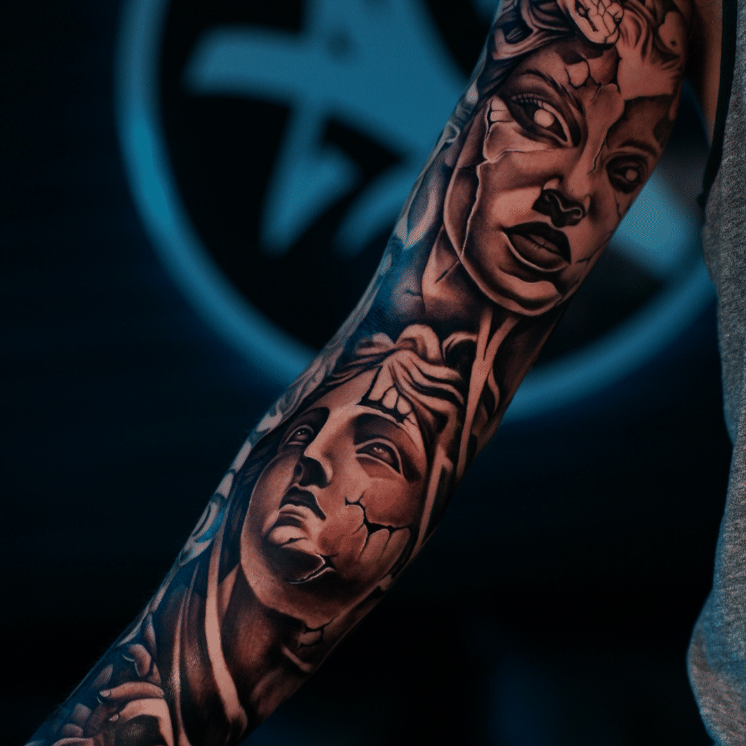Black and grey full inner arm sleeve of two cracked classical statue faces, one gazing upward, Tagz Tattoo in Mesa, AZ