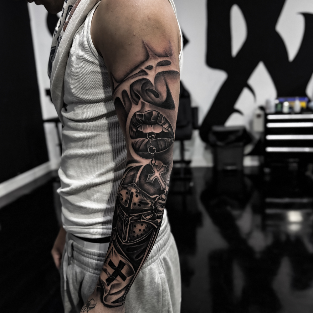 Black and grey full arm sleeve with lips, a cross pendant and a crusader helmet, Tagz Tattoo in Mesa, AZ